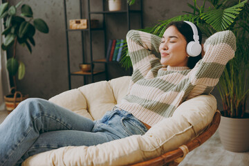 Side view young calm woman wear casual clothes listen music in headphones close eyes sit on...