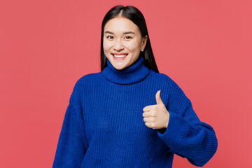 Young smiling happy cheerful woman of Asian ethnicity she wearing blue sweater casual clothes showing thumb up like gesture isolated on plain pastel pink background studio portrait. Lifestyle concept.