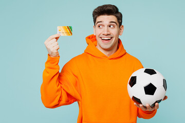 Young fun man fan wears orange hoody casual clothes show credit bank card look aside cheer up...