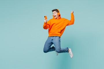 Full body side view young man he wearing orange hoody casual clothes jump high use hold mobile cell...