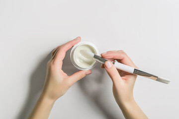 female hands picking up a cosmetic mask from a bottle with a brush, top view