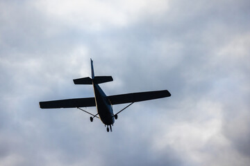 Light aircraft silhouette is in cloudy sky on a daytime, rear view