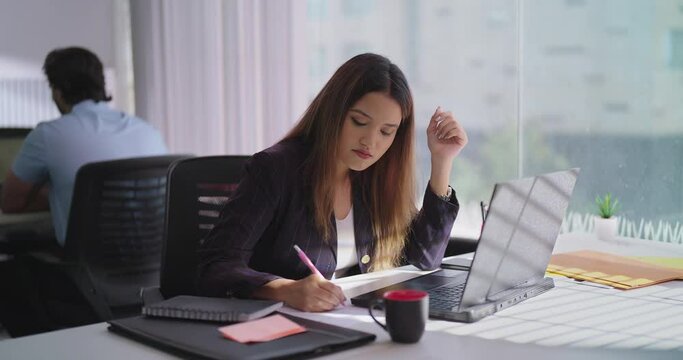 Indian Asian young adult busy lady staff business woman sitting desk chair indoor job home office use laptop focused hindu female girl worker do work study task typing online email look webcam screen
