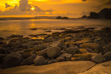 Sunset at the rocky beach in Papuma, Jember, East Java, Indonesia. Cloudy afternoon with ocean waves swipe the sands. Nature and Landscape Photography.