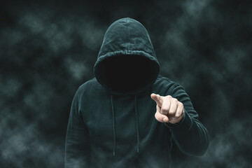 Mysterious faceless hooded anonymous criminal, silhouette of computer hacker, cyber terrorist or gangster on black background with smoke