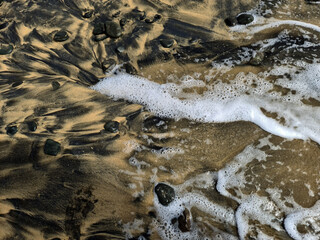 Beautiful black and brown sand beach with stones and water. Close up abstract image.
