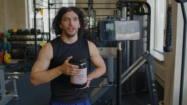 Medium shot of male fitness trainer telling about protein supplement for sportsmen on smartphones camera in tripod