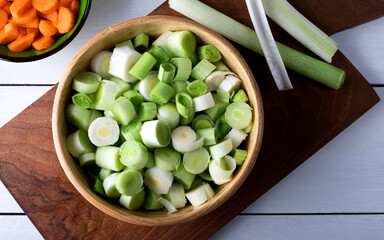 Chopped leeks in a wooden bowl on a cutting board