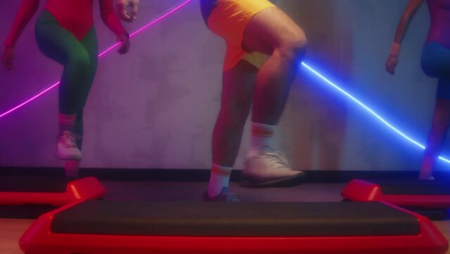 Cropped shot of unrecognizable people doing knee-up steps while practicing aerobics in studio with neon lights