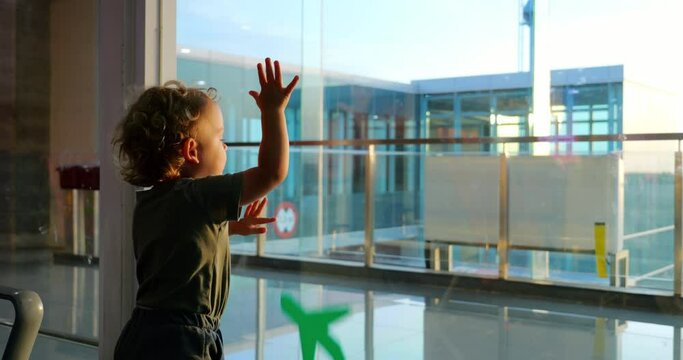 Toddler plays with model airplane in airport. He presses green toy against window, inadvertently or intentionally drops it, and then, in oddly deliberate and slightly unsettling moment