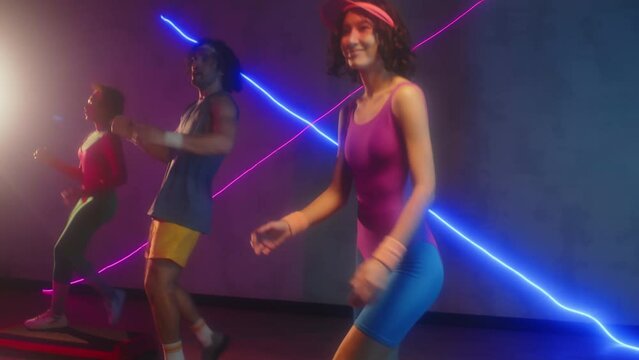 Tilt up shot of three active sportspeople practicing steps during aerobics class in retro style in studio with neon lights