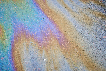 Multi-colored poisonous spots of spilled gasoline on wet pavement during rain.