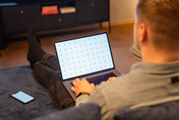 Young casual man looking at his laptop while working from home office - obrazy, fototapety, plakaty
