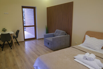 Modern design of a living room in a hotel. Chair, bed, table. Exit to a balcony with a transparent glass door.