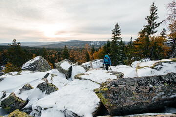 a girl with backpacks walks on rocks in the snow