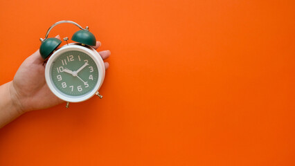 Hand holds classic green alarm clock on orange background with a copy space - obrazy, fototapety, plakaty