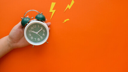 Hand holds ringing classic green alarm clock on orange background with a copy space - obrazy, fototapety, plakaty