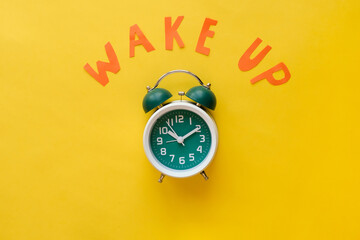 Classic green alarm clock with a text Wake up on yellow background - obrazy, fototapety, plakaty