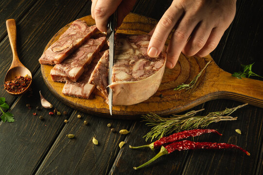Chef cuts brawn into pieces with a knife on a kitchen wooden board before preparing breakfast sandwiches. Quick snack concept with headcheese and aromatic spices