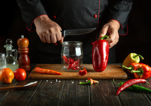 A cook cans peppers in a jar on a restaurant kitchen table. The concept of preparing vegetables for the winter.