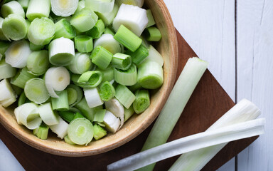 Chopped leek in a wooden bowl on white wooden background.