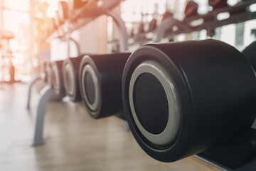 A black dumbbell on a shelf inside a gym or exercise facility has light shining from a mirror...