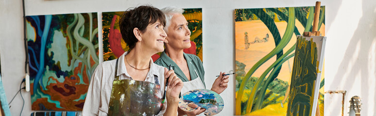 joyful creative mature women in aprons looking away in modern art workshop, horizontal banner