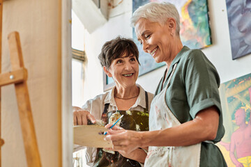 Obraz premium cheerful middle aged female artists mixing paints on palette during master class in art workshop