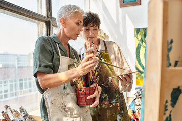 talented mature female artists choosing  paintbrushes during master class in craft workshop