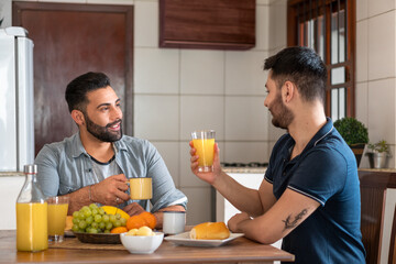 brazilian gay couple having breakfast and talking in kitchen table - obrazy, fototapety, plakaty
