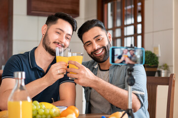 happy gay couple celebrating and recording video with mobile in kitchen table