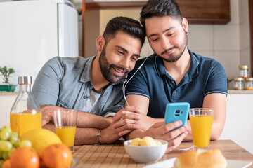 romantic gay couple using mobile phone and watching video together in kitchen table