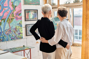 back view of elegant lesbian couple of artists embracing and standing in modern art workshop