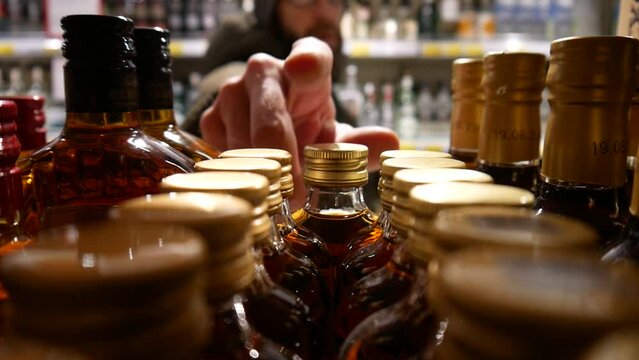 Close-up of many beautiful bottles of whiskey and brandy in alcohol store and a male buyer chooses one.