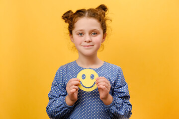 Portrait of smiling pretty preteen girl child holding small paper happy emoticon, posing isolated...