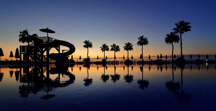 Wasserpark und Pool Sonnenaufgang mit Spiegelung auf dem Wasser, Palmen und Sonnenschirme im Hintergrund