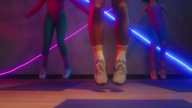 Cropped shot of active people performing jumps while doing aerobics at studio with neon lights