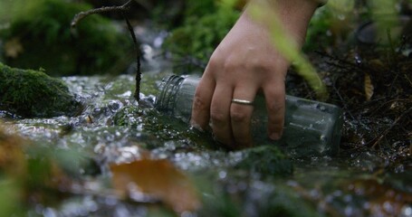 Close up shot of greenery and flowing clear stream in beautiful forest. Tourist comes to gather water from creek into bottle. Traveler during trek or expedition in mountains. Nature discovery concept.