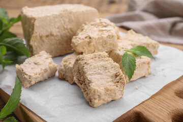 Pieces of tasty halva and mint leaves on table, closeup