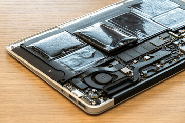 Swollen battery of broken laptop in open casing closeup. Heavy damage of notebook computer diagnostics in repair service. Problem with pc