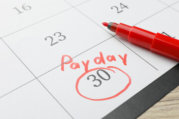 Calendar page with marked payday date and red marker on table, closeup