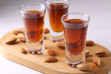 Shot glasses with tasty amaretto liqueur and almonds on white wooden table, closeup