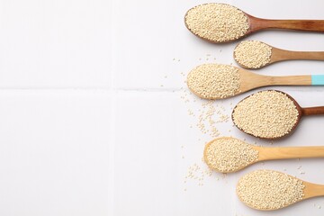 Spoons with dry quinoa seeds on white tiled table, flat lay. Space for text