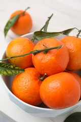 Fresh ripe tangerines and leaves in bowl on white table, closeup