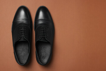 Pair of leather men shoes on brown background, top view. Space for text