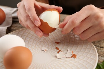 Woman peeling boiled egg at wooden table, closeup