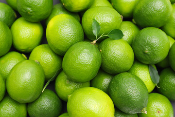 Many fresh limes with green leaves as background, top view