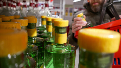 Close-up of many beautiful green glass bottles of gin or absinthe on a supermarket shelf and a male...