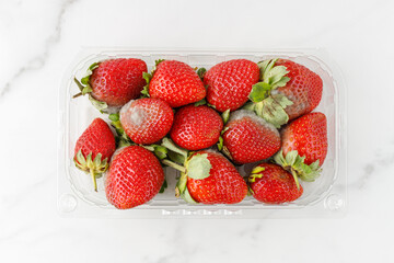 Spoiled strawberry berries with mold  in transparent plastic box closeup isolated on white marble...