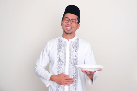 Moslem man touching his stomach with happy relieved expression while holding empty dinning plate